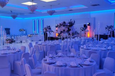 Salle de réception élégante avec un arc floral blanc, des tables décorées et un éclairage lumineux.