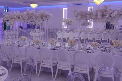 Salle de réception élégante avec un arc floral blanc, des tables décorées et un éclairage lumineux.