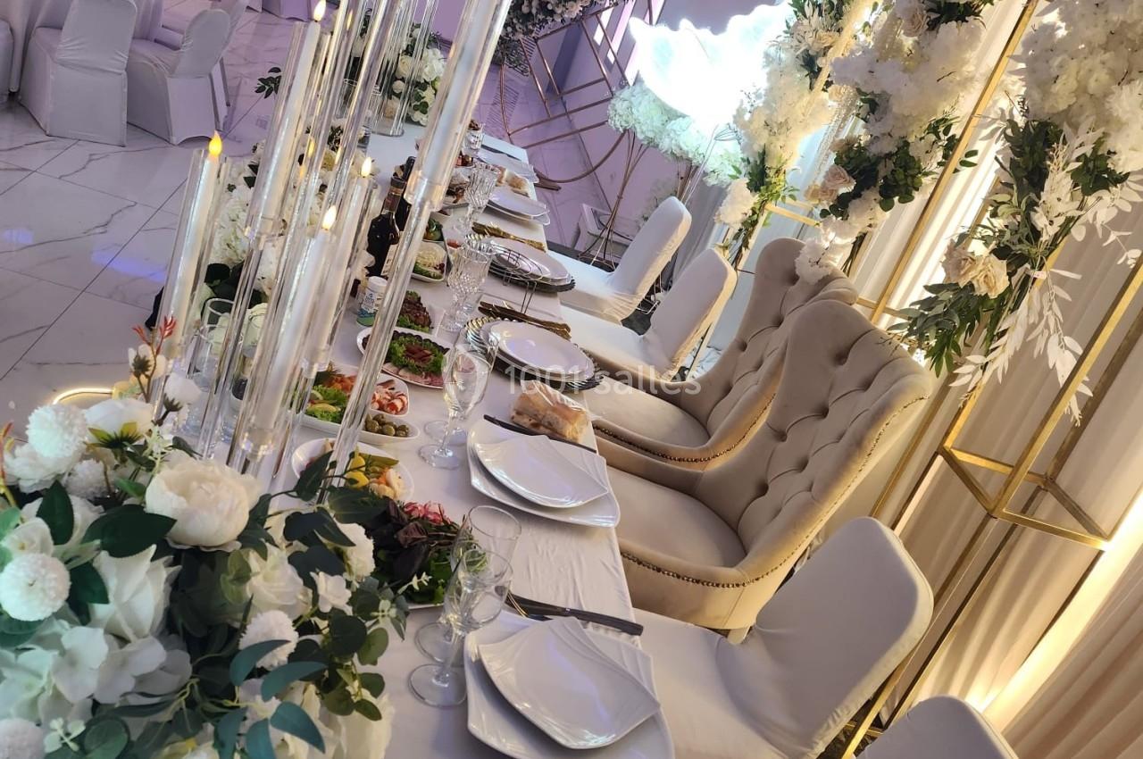 Table de réception élégamment décorée avec des fleurs blanches, des chandeliers et des assiettes dressées.