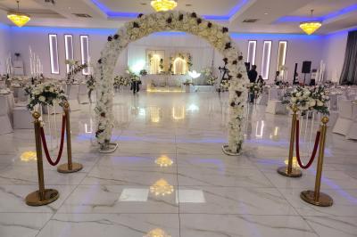 Salle de réception élégante avec un arc floral blanc, des tables décorées et un éclairage lumineux.