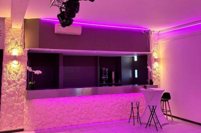 Salle de réception décorée avec des tables rondes, nappes blanches, chaises élégantes et éclairage violet tamisé.