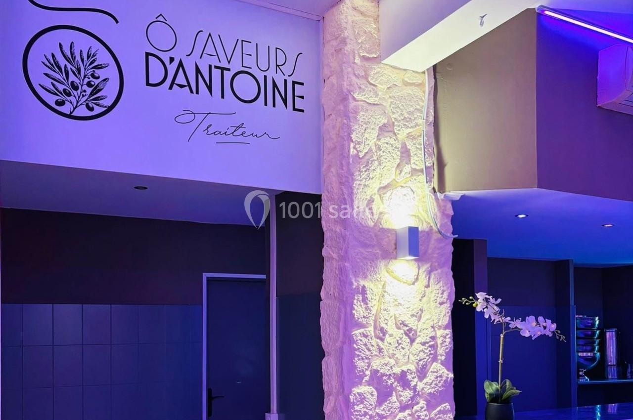 Intérieur d'un restaurant avec mur texturé, éclairage violet et logo ’Ô Saveurs d'Antoine Traiteur’ visible.