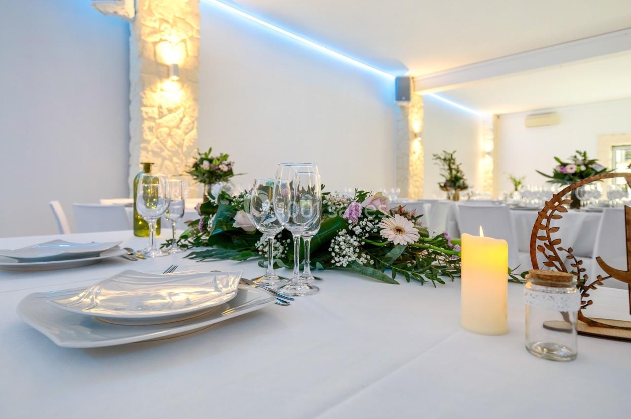 Table décorée avec des assiettes blanches, verres, bougie et centre de table floral dans une salle lumineuse.