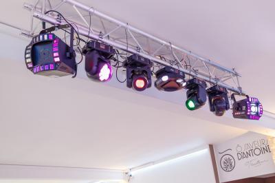 Salle de réception décorée avec des tables rondes, nappes blanches, chaises élégantes et éclairage violet tamisé.