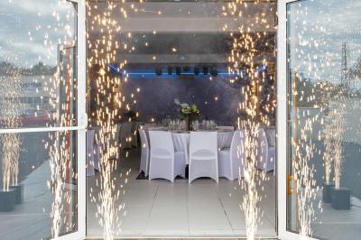 Salle de réception décorée avec des tables rondes, nappes blanches, chaises élégantes et éclairage violet tamisé.