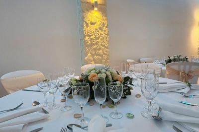 Salle de réception décorée avec des tables rondes, nappes blanches, chaises élégantes et éclairage violet tamisé.