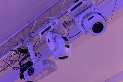 Salle de réception décorée avec des tables rondes, nappes blanches, chaises élégantes et éclairage violet tamisé.