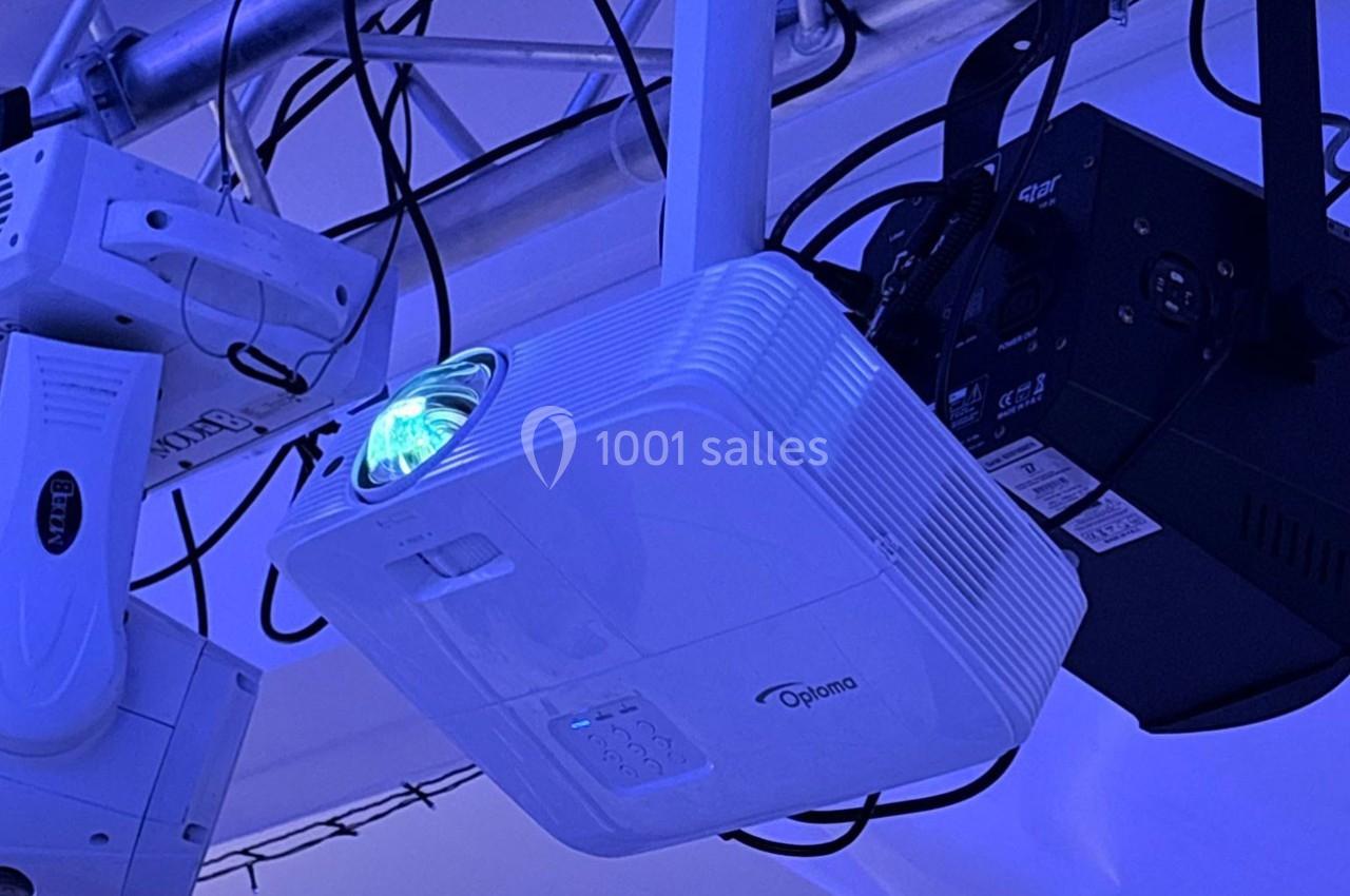 Projecteur blanc fixé à une structure métallique, émettant une lumière bleue dans un environnement sombre.