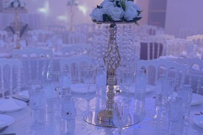 Salle de réception décorée avec des tables rondes, nappes blanches, chaises élégantes et éclairage violet tamisé.