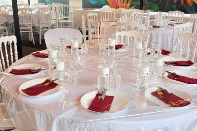 Salle de réception décorée avec des tables rondes, nappes blanches, chaises élégantes et éclairage violet tamisé.