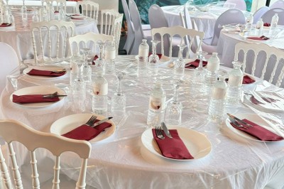 Salle de réception décorée avec des tables rondes, nappes blanches, chaises élégantes et éclairage violet tamisé.
