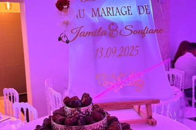 Salle de réception décorée avec des tables rondes, nappes blanches, chaises élégantes et éclairage violet tamisé.