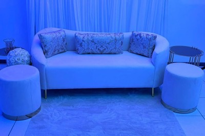 Salle de réception décorée avec des tables rondes, nappes blanches, chaises élégantes et éclairage violet tamisé.