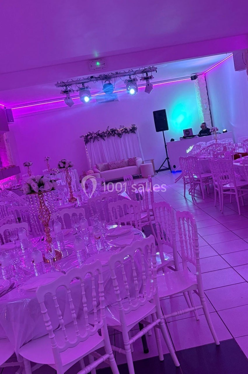Salle de réception décorée avec des tables dressées, des chaises blanches et un éclairage rose.
