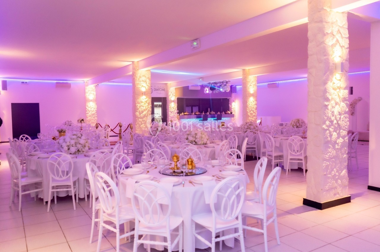 Salle de réception lumineuse avec tables rondes décorées de nappes blanches et centres de table floraux.