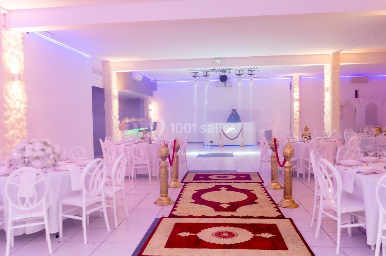 Salle de réception décorée avec des tables dressées, un tapis rouge central et une piste de danse éclairée.