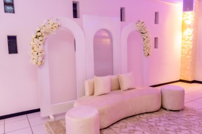 Salle de réception décorée avec des tables rondes, nappes blanches, chaises élégantes et éclairage violet tamisé.