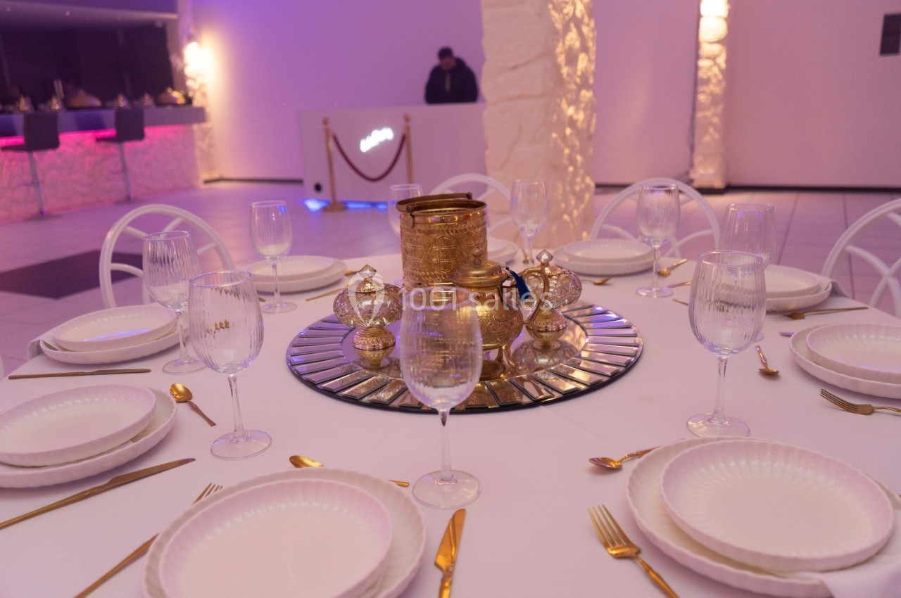 Table dressée avec vaisselle blanche, couverts dorés et centre de table en métal doré sur un plateau miroir.