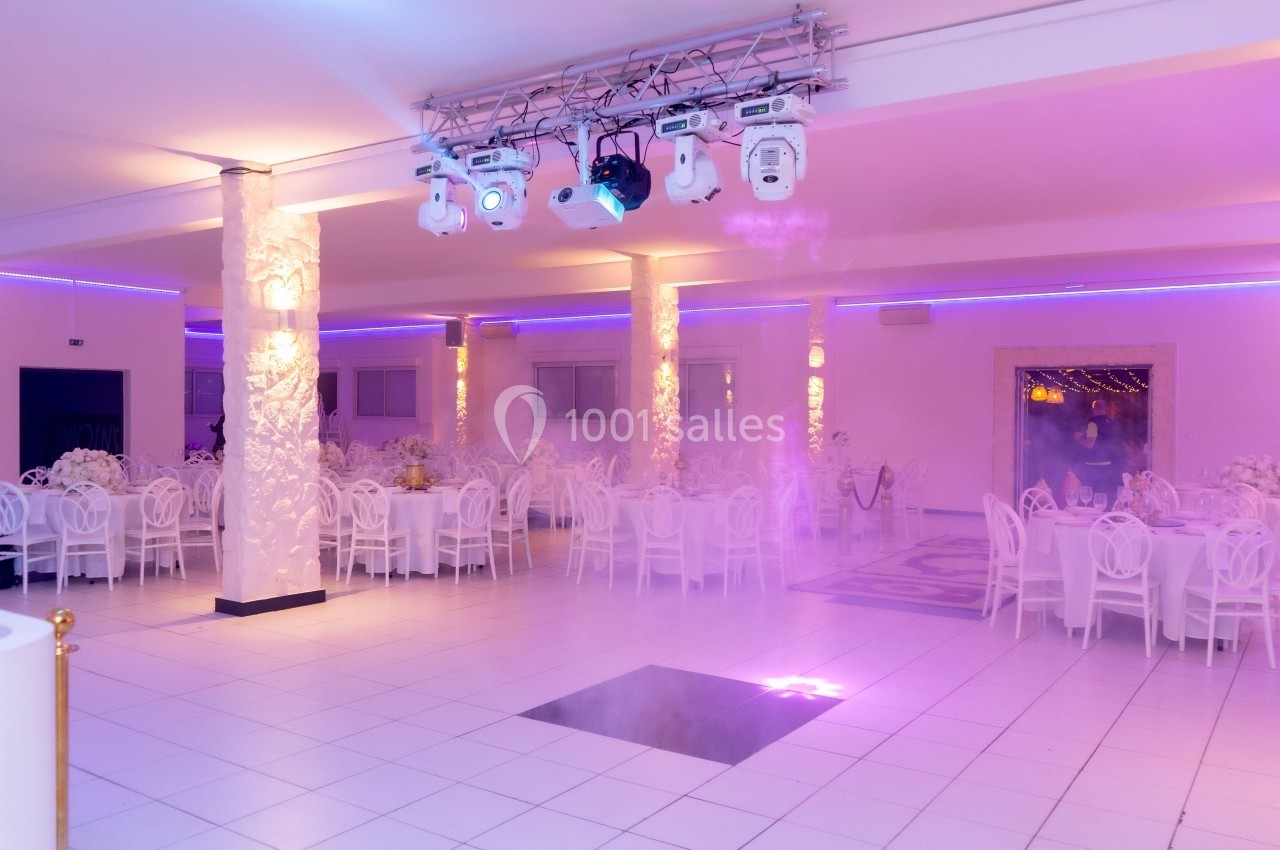 Salle de réception lumineuse avec décoration blanche, tables dressées et éclairage violet.