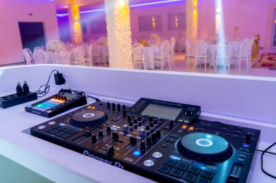 Salle de réception décorée avec des tables rondes, nappes blanches, chaises élégantes et éclairage violet tamisé.