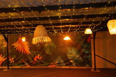 Salle de réception décorée avec des tables rondes, nappes blanches, chaises élégantes et éclairage violet tamisé.