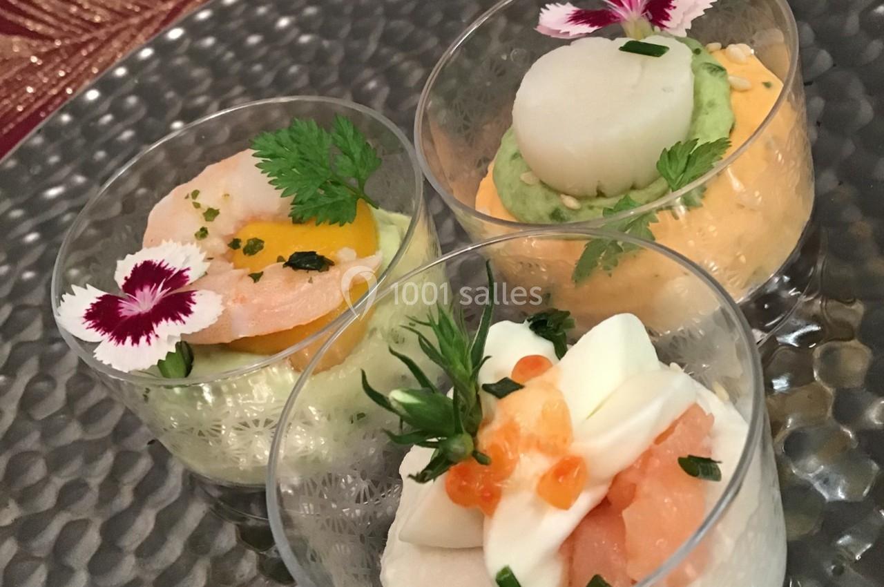 Trois verrines garnies de crevettes, saumon, purées colorées et décorations florales sur un plateau métallique.