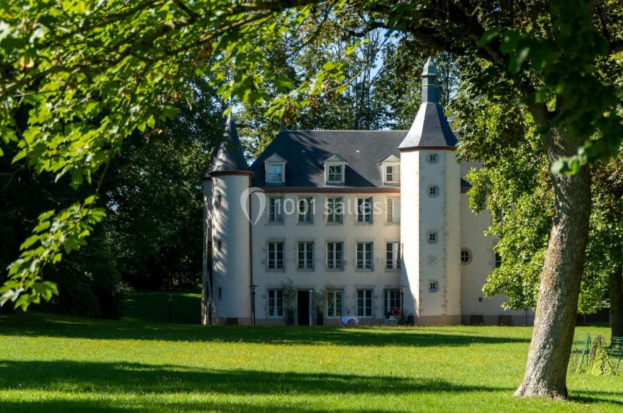 Façade d'un petit château blanc entouré d'arbres et d'une pelouse verdoyante sous un ciel dégagé.