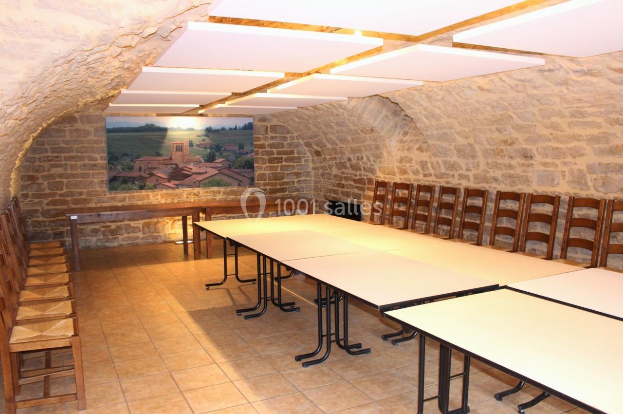 Salle voûtée en pierre avec tables et chaises en bois, éclairée par des panneaux lumineux au plafond.