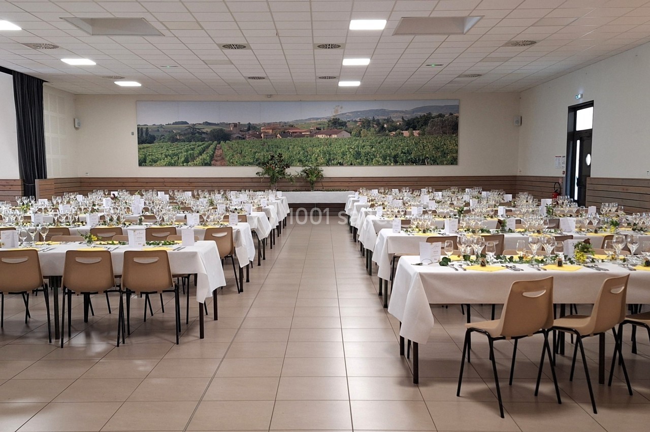 Salle de réception avec tables dressées pour un événement, décorée de nappes blanches et de centres de table fleuris.