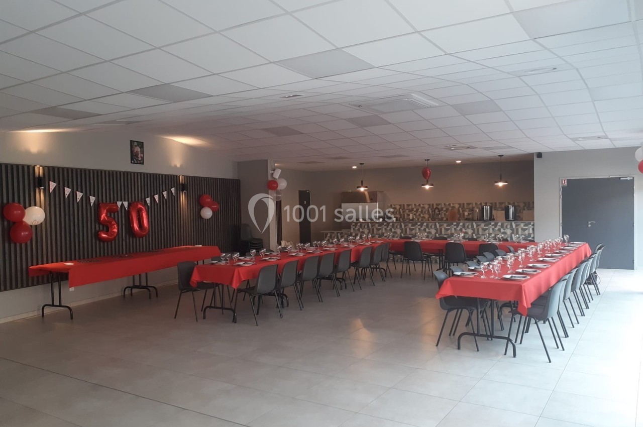 Salle décorée pour un 50e anniversaire, avec tables alignées, nappes rouges et ballons suspendus.