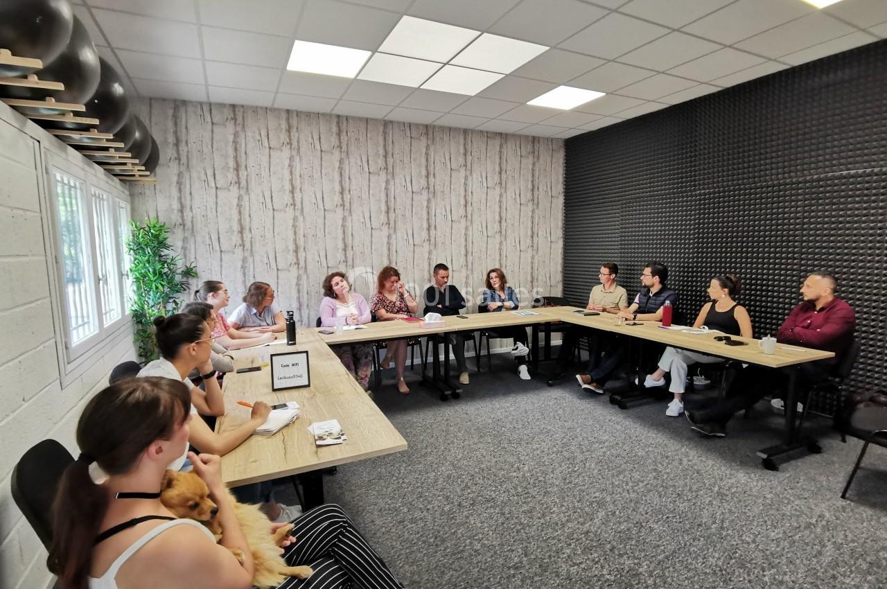 Un groupe de personnes assises autour de tables en réunion dans une salle lumineuse avec un mur en bois et un autre…