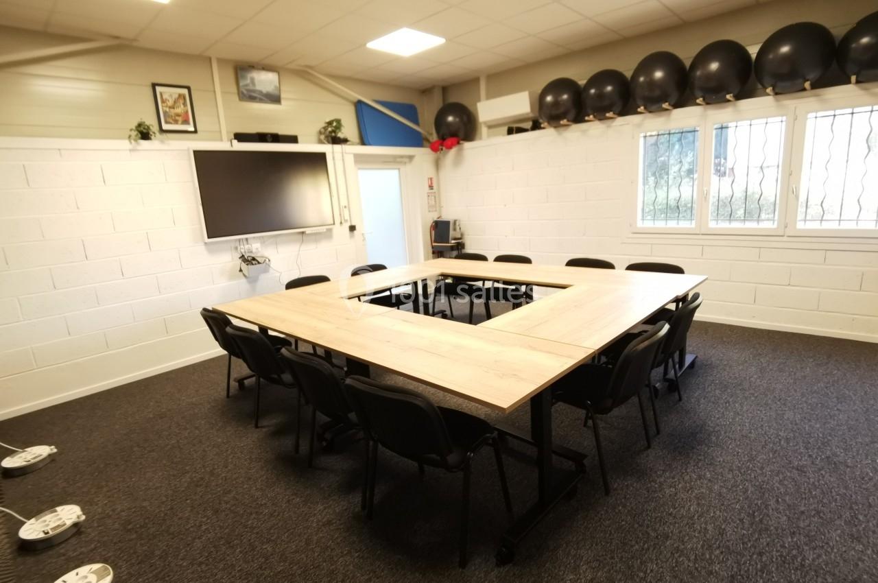 Salle de réunion avec table en U, chaises noires, écran mural, fenêtres et ballons de fitness alignés sur une étagère.
