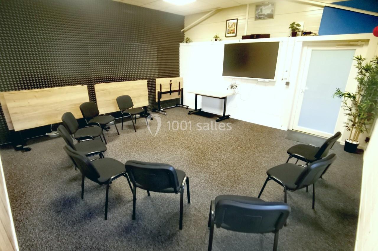 Salle de réunion avec des chaises disposées en cercle, un écran mural et des panneaux acoustiques noirs.
