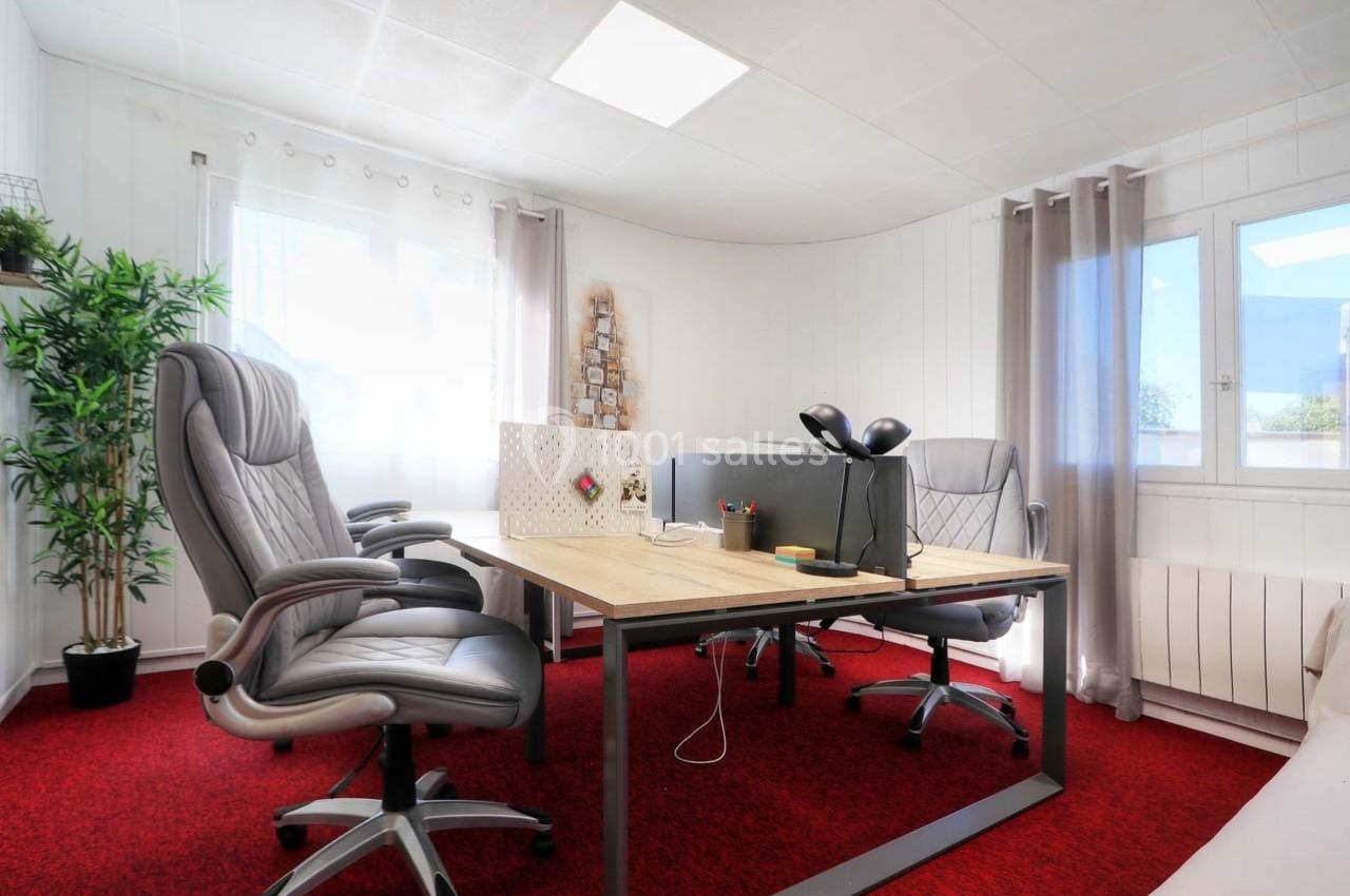Bureau lumineux avec deux fauteuils gris, une table en bois, un séparateur de bureau et une fenêtre donnant sur l'extérieur.