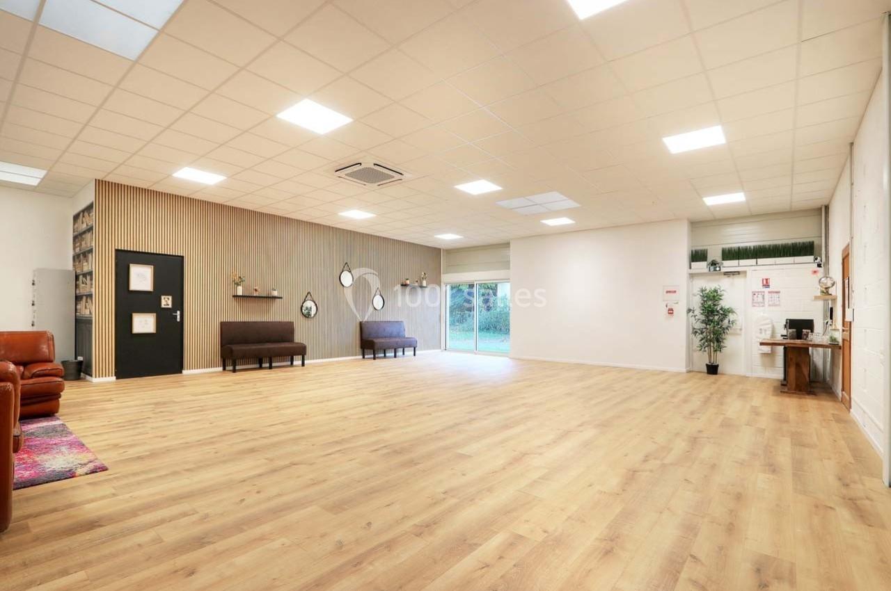 Salle spacieuse avec parquet clair, murs décorés, canapés, étagères et grande baie vitrée donnant sur l'extérieur.