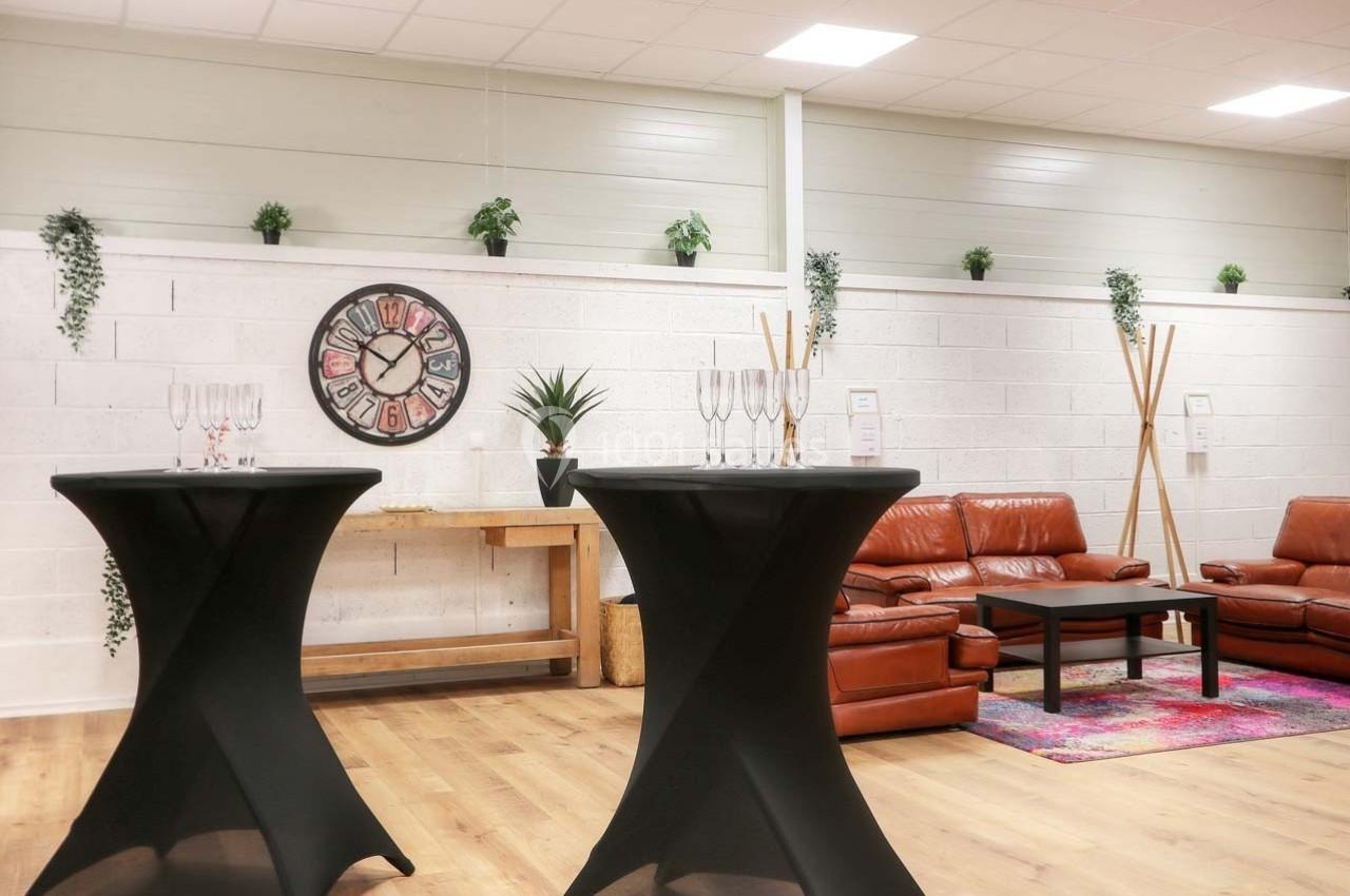 Salle lumineuse avec canapés en cuir, tables hautes noires, décorations murales et plantes suspendues.