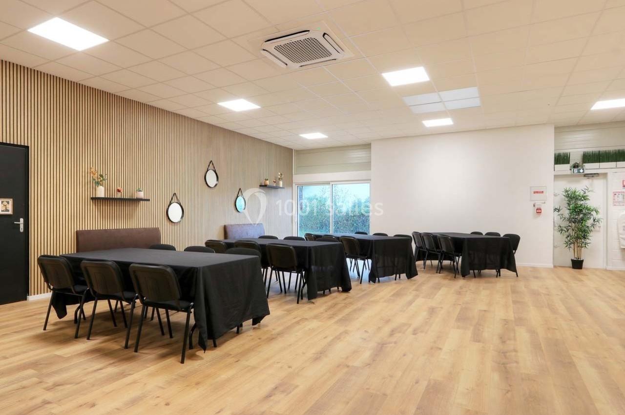 Salle lumineuse avec parquet, tables noires alignées, chaises, murs clairs et décorations murales modernes.