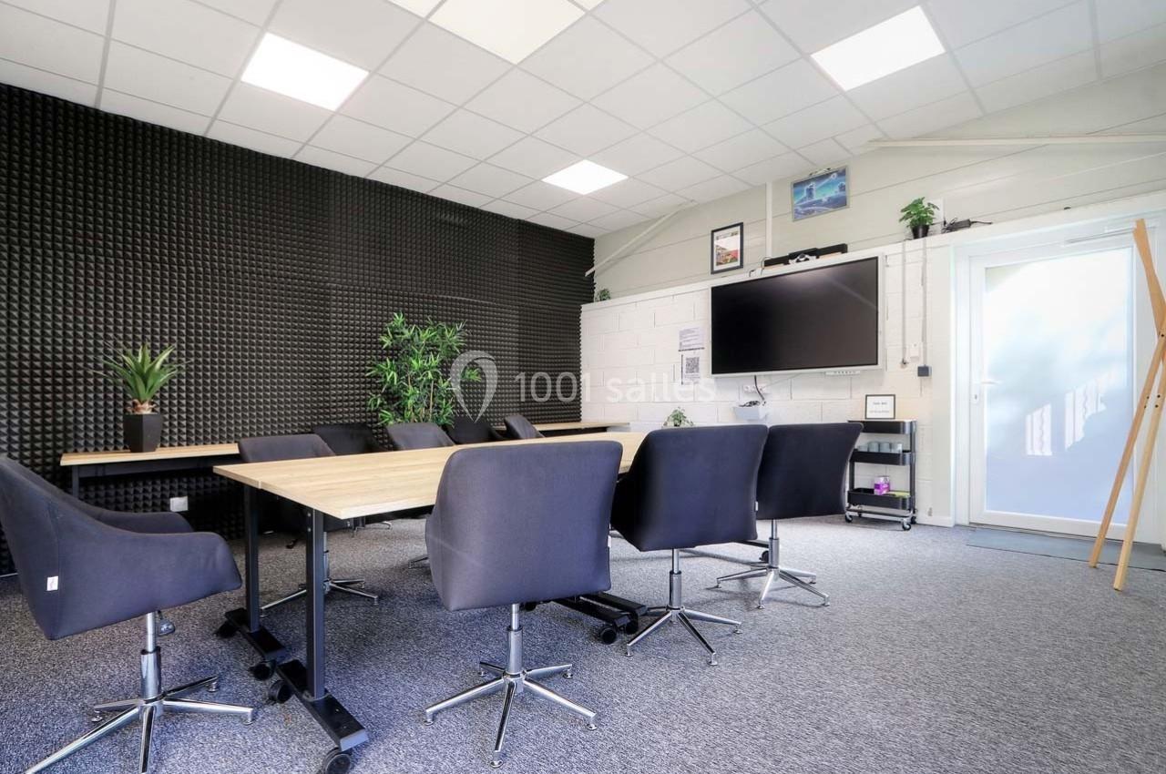 Salle de réunion moderne avec table en bois, chaises noires, écran mural et plantes décoratives.
