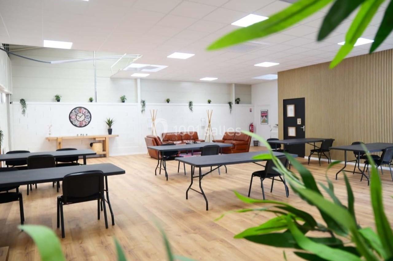 Salle lumineuse avec parquet, tables et chaises noires, canapés en cuir marron et plantes en décoration.