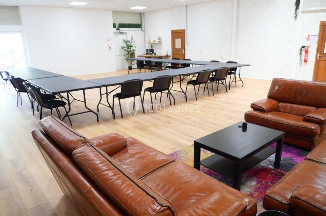 Salle lumineuse avec tables de réunion noires, chaises, canapés en cuir marron et sol en parquet clair.