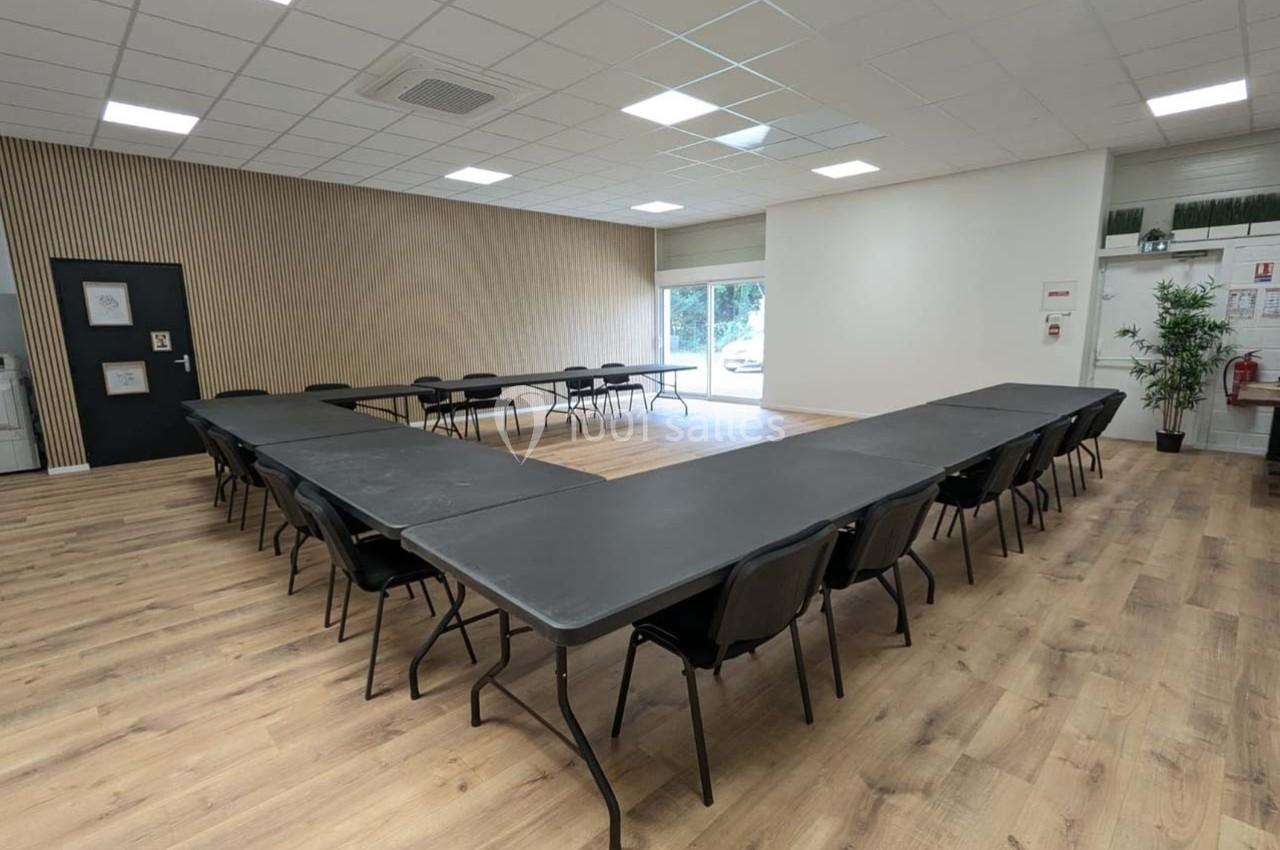 Salle de réunion lumineuse avec tables disposées en U, chaises noires et sol en parquet clair.