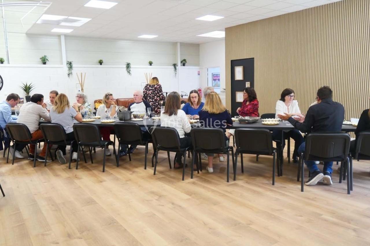 Des personnes assises autour de longues tables dans une salle lumineuse, partageant un repas ou une discussion.