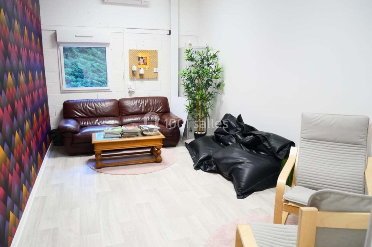 Salon lumineux avec canapé en cuir, fauteuils, poufs noirs, table basse en bois et mur décoratif coloré.