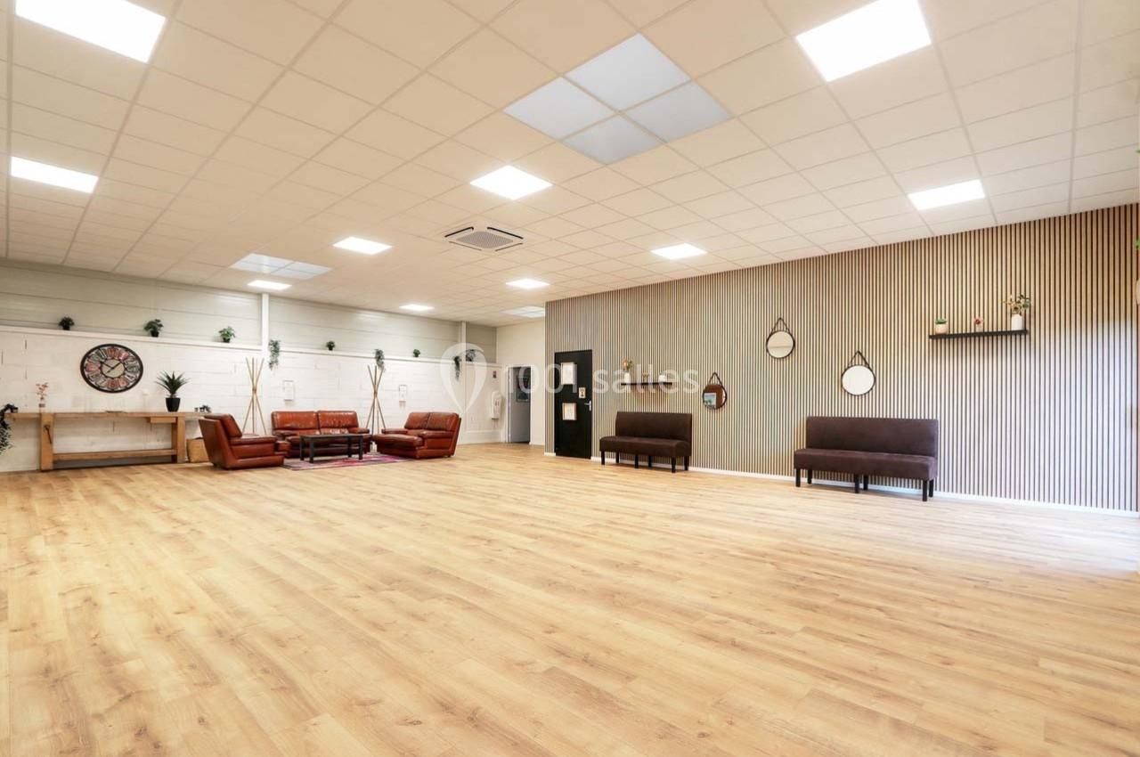 Salle spacieuse avec parquet clair, murs décorés de miroirs et étagères, et mobilier en cuir et bois.