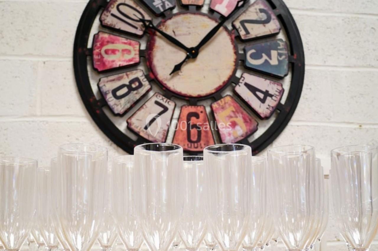 Horloge murale décorative avec chiffres colorés en arrière-plan, alignée au-dessus de verres à pied transparents.