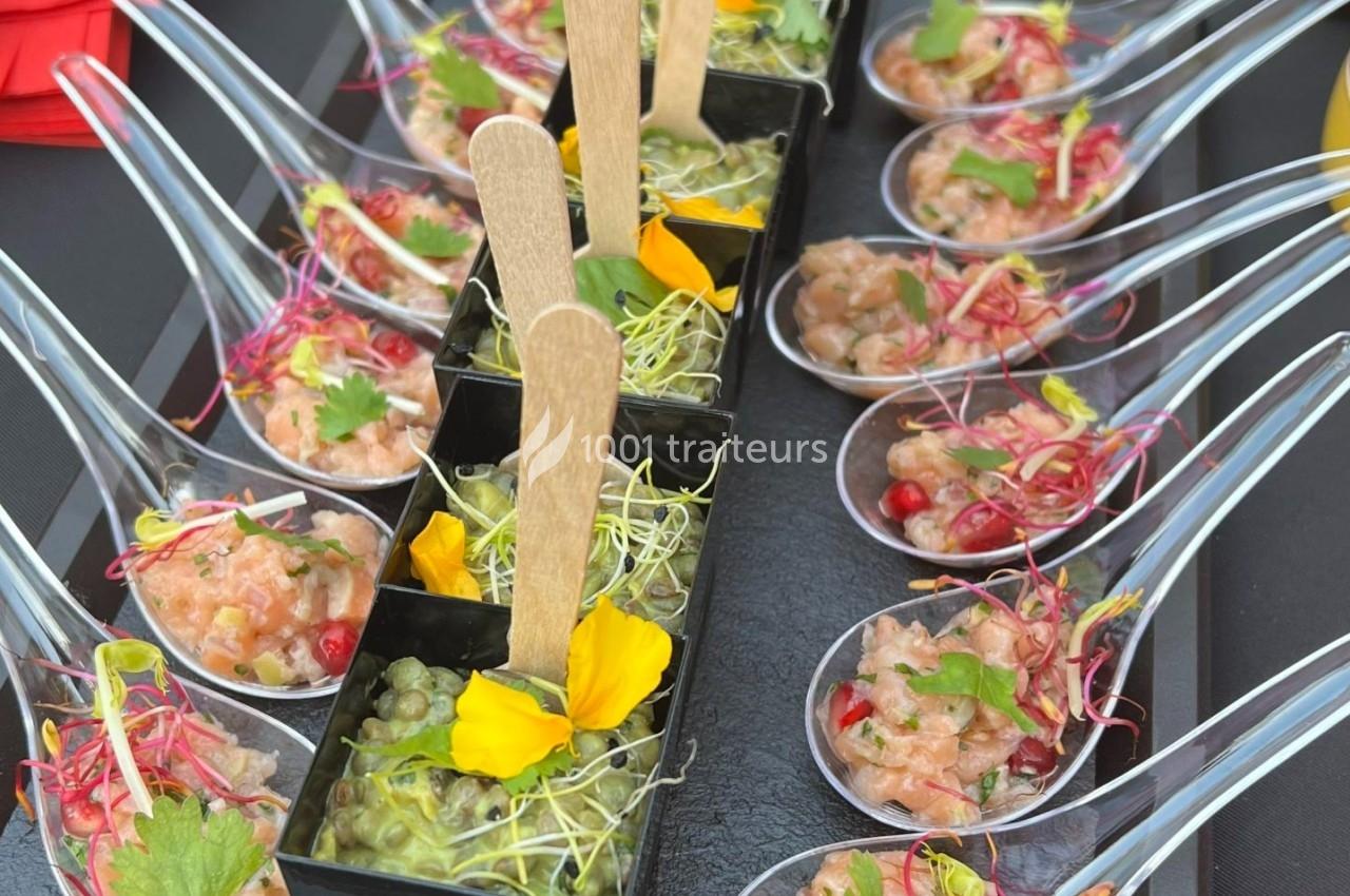 Cuillères apéritives garnies de tartare de saumon et verrines de guacamole décorées de fleurs comestibles.