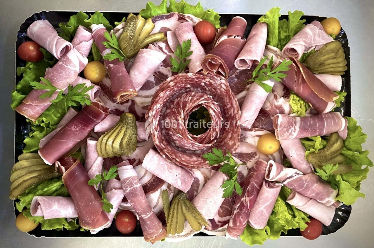 Plateau de charcuterie avec jambon, saucisson, cornichons, tomates cerises et feuilles de salade en décoration.