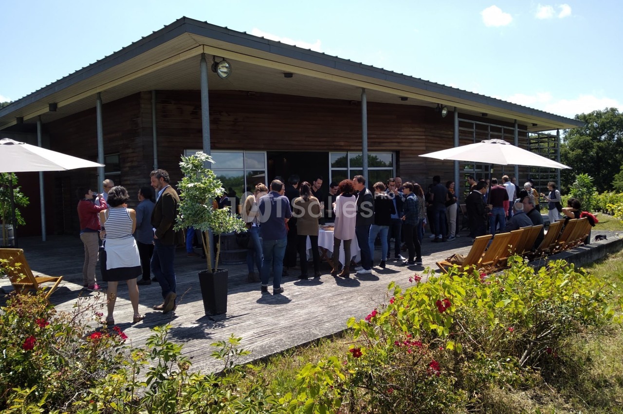 Groupe de personnes rassemblées sur une terrasse en bois devant un bâtiment moderne, entouré de végétation.