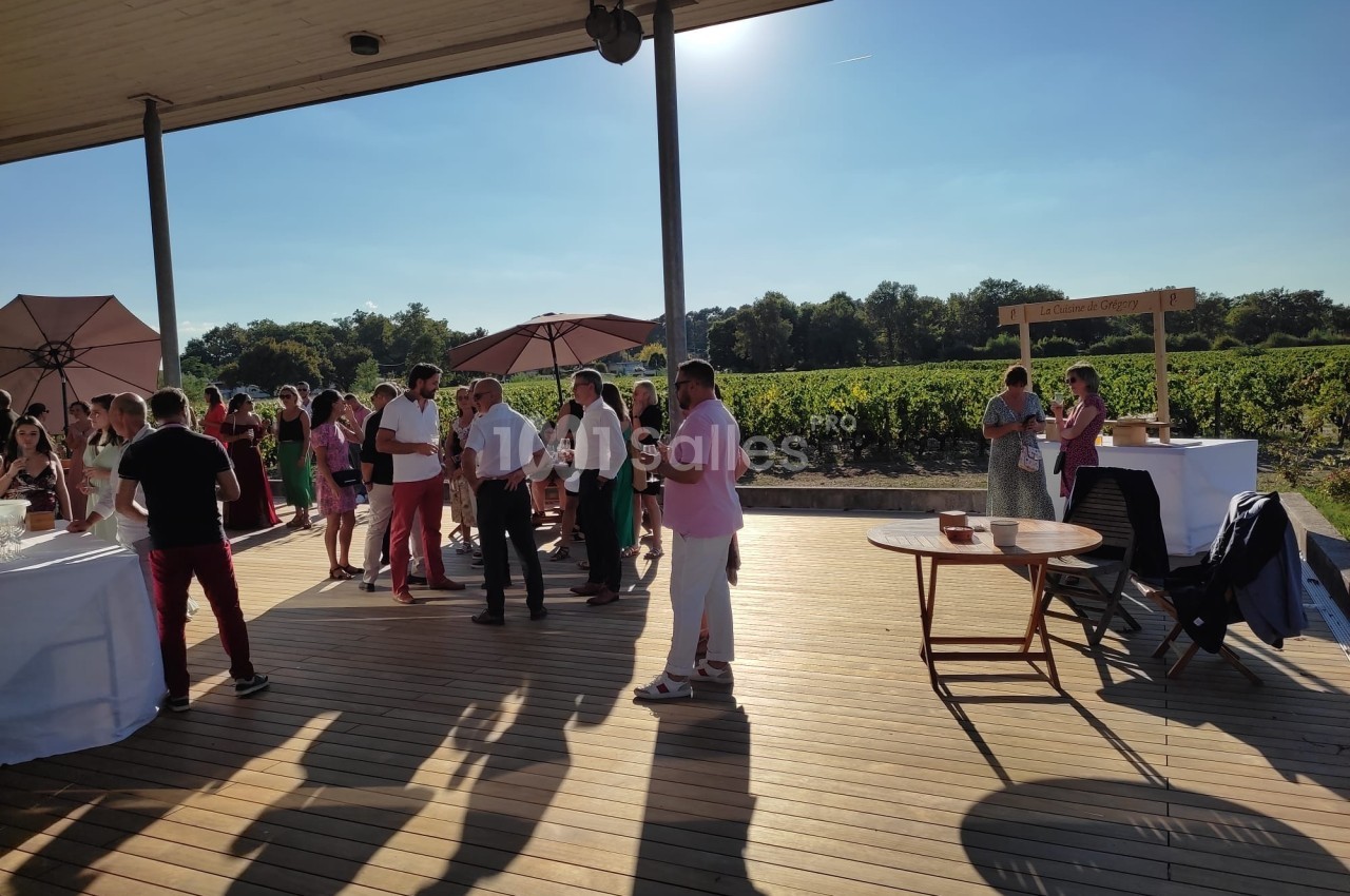 Personnes rassemblées sur une terrasse en bois, près de vignobles, sous un ciel dégagé en fin de journée.