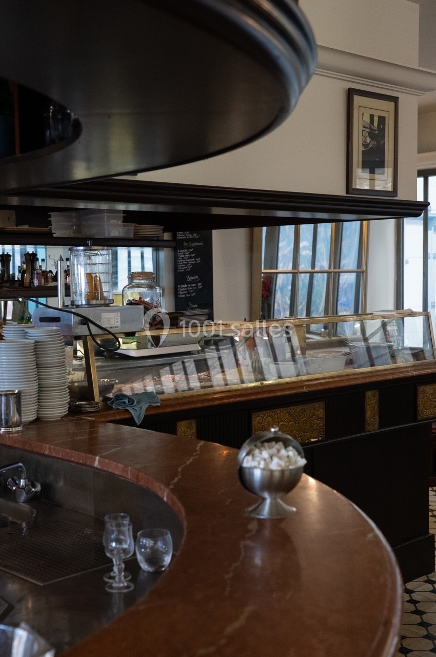 Comptoir de café avec vaisselle empilée, vitrine réfrigérée et décor intérieur lumineux.